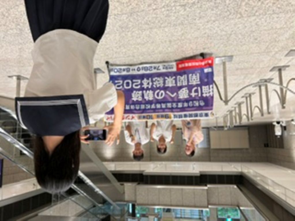 横断幕の前でポーズをとって写真撮影をする様子の写真